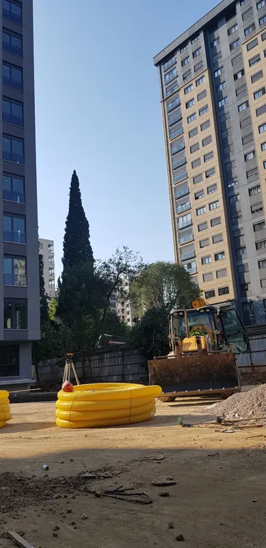 Apartmanlar arasındaki kazı alanında iş makinesi ve boru malzemeleri